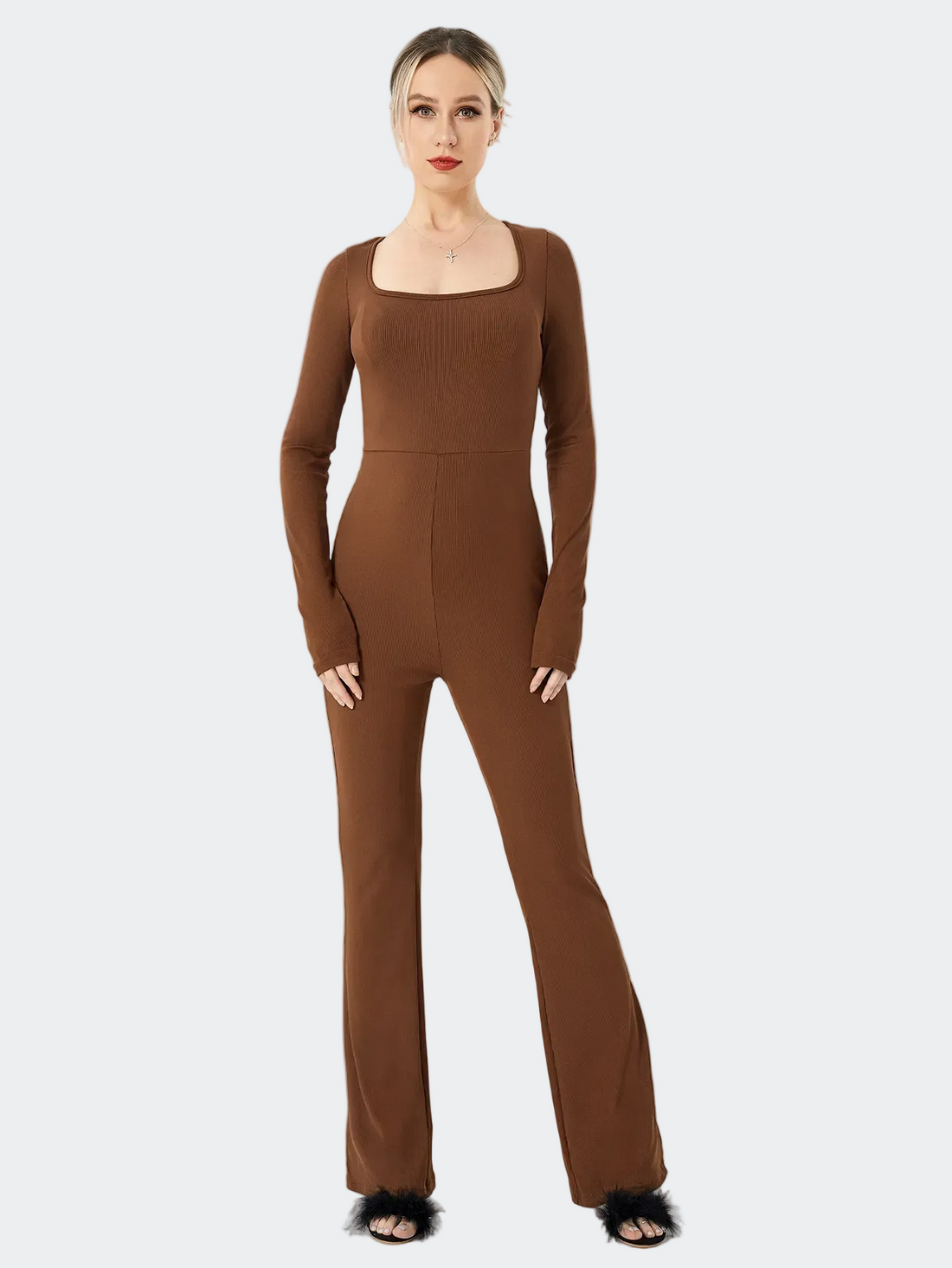 A woman modeling a long-sleeve, square-neck jumpsuit in a solid medium brown color, standing against a plain white studio background.
