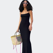 Woman in a black dress holding a straw bag against a pink wall.