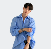 A man wearing a light blue long-sleeve button-up shirt with thin white vertical stripes, posed in a modern indoor setting.